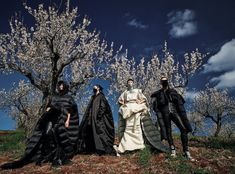 four people dressed in black and white are posing for a photo near some flowering trees