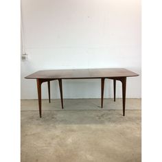 a wooden table sitting on top of a cement floor next to a white wall in an empty room