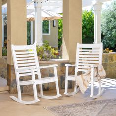 two white rocking chairs sitting next to each other on top of a stone patio area