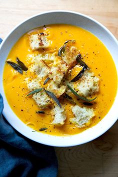 a white bowl filled with soup and croutons on top of a wooden table