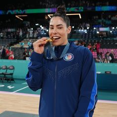 a woman holding a medal while standing on top of a basketball court