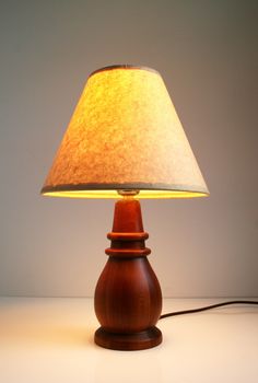 a wooden table lamp with a white shade on the base and a cord attached to it