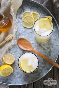 two glasses filled with lemonade and honey sit on a metal tray next to wooden spoons