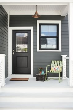 a green chair sitting on the front steps of a gray house next to a black door