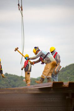 three men in hard hats and safety vests are working on a roof with a crane