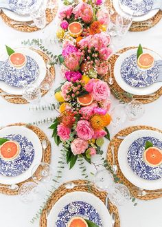 the table is set with blue and white plates, oranges, and pink flowers