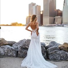 a woman in a white wedding dress standing on rocks near the water with her back to the camera