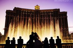 a bride and groom are standing in front of the fountains of water at night with their arms around each other