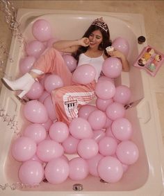 a woman laying in a bathtub filled with pink balloons