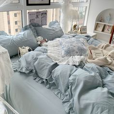 an unmade bed with blue sheets and pillows in front of a window overlooking the city