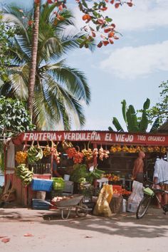 a fruit and vegetable stand on the side of the road with palm trees in the background