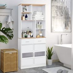 a bathroom with white cabinets and towels on the shelves next to a bathtub, towel rack, toilet paper dispenser and potted plant