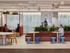 people sitting at tables in an office setting with plants on the wall and couches