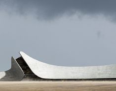 a large white building sitting in the middle of a field under a gray sky with dark clouds