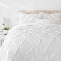 a bed with white comforter and pillows on it in front of a brick wall