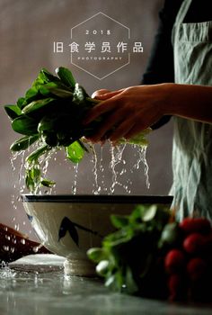 a person is sprinkling water from a bowl filled with green leaves and vegetables