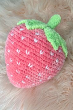 a crocheted strawberry with green leaves on it's side sitting on a furry surface