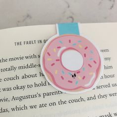 a pink donut with sprinkles sitting on top of an open book