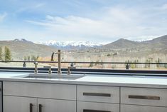 a kitchen sink sitting next to a window with mountains in the background