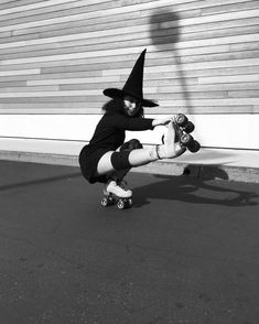 a woman riding a skateboard down the side of a road wearing a witches hat