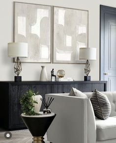 a living room filled with white furniture and two paintings on the wall above each couch