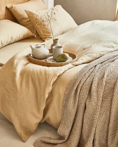 a tray with two teapots sitting on top of a bed next to pillows