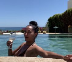 a woman holding a wine glass next to a swimming pool with the ocean in the background