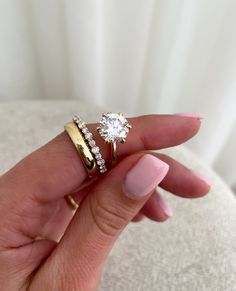 a woman's hand holding two gold rings with diamonds on each one and the other side