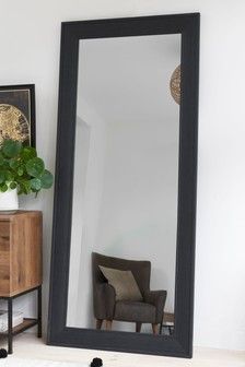 a large black framed mirror sitting on top of a wooden table next to a chair