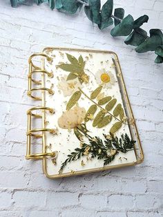 an open notebook with pressed flowers and leaves on it next to a garland of greenery