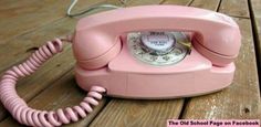 an old pink phone sitting on top of a wooden table