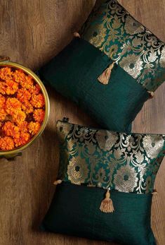 two decorative pillows with tassels on them next to a bowl of food that is sitting on the floor