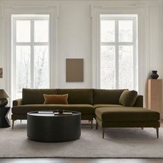 a living room with two large windows and a sectional couch in the middle, along with a coffee table