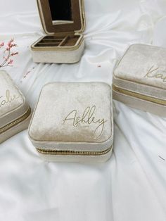 three personalized jewelry cases sitting on a white cloth covered bed with flowers in the background