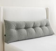 a close up of a bed with a white headboard and pillows on top of it