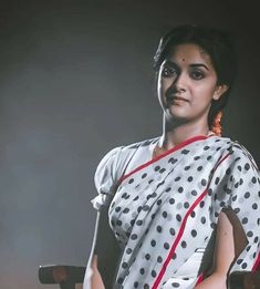 a woman sitting in a chair wearing a polka dot sari with red trim around her neck