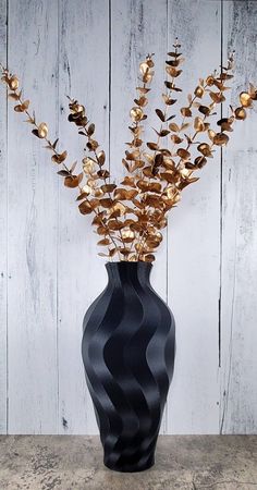 a black vase with gold flowers in it sitting on a stone table next to a wooden wall