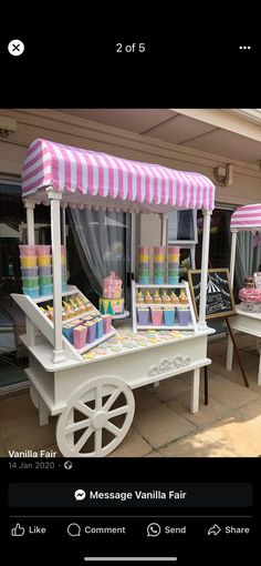 an ice cream cart with pink and white striped awnings on the top is selling cupcakes