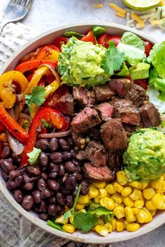 a bowl filled with meat, vegetables and guacamole on top of a table