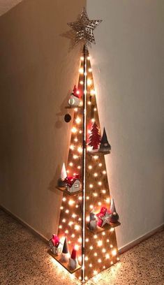 a christmas tree with lights and decorations on the top is in front of a wall