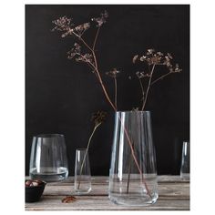 three glass vases with flowers in them on a wooden table next to a black wall