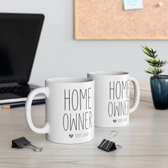 two coffee mugs sitting on top of a wooden table next to a laptop computer