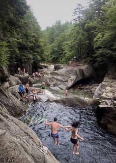 some people are standing in the water near rocks and trees with their arms out to each other