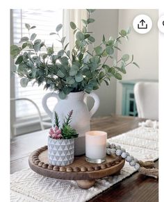 a white vase filled with greenery sitting on top of a wooden tray next to a candle