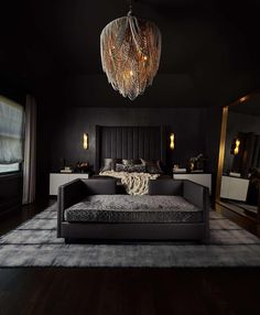 a black bedroom with a large bed and chandelier hanging from it's ceiling