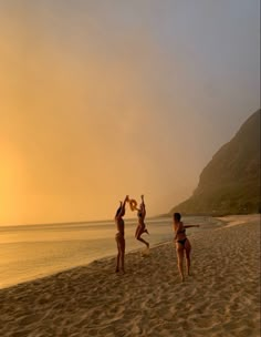 three people jumping up in the air on a beach at sunset with mountains in the background