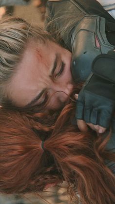 a woman with red hair and gloves laying on the ground next to an iron man