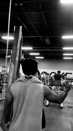 a man in a gym holding up a pole with other people working out behind him