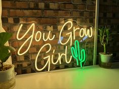 a neon sign that says you grow girl next to a potted plant