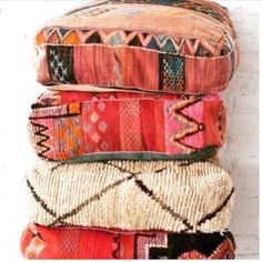 a stack of colorful pillows sitting on top of a white table next to a brick wall